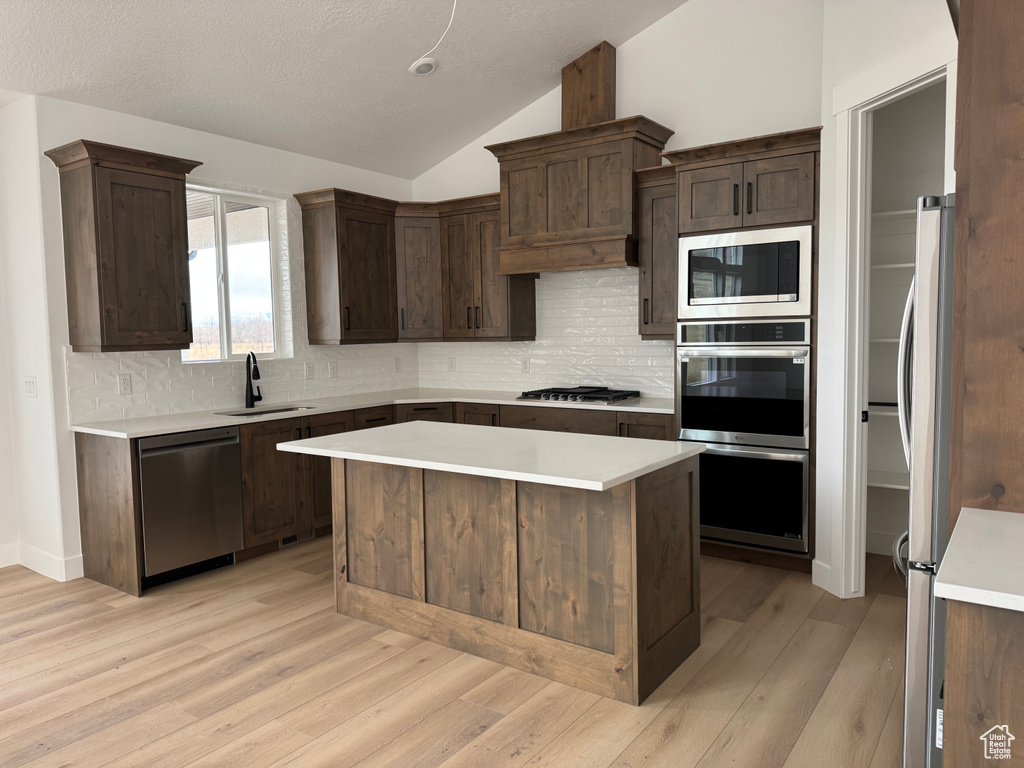 Kitchen featuring sink, vaulted ceiling, light hardwood / wood-style floors, a kitchen island, and stainless steel appliances