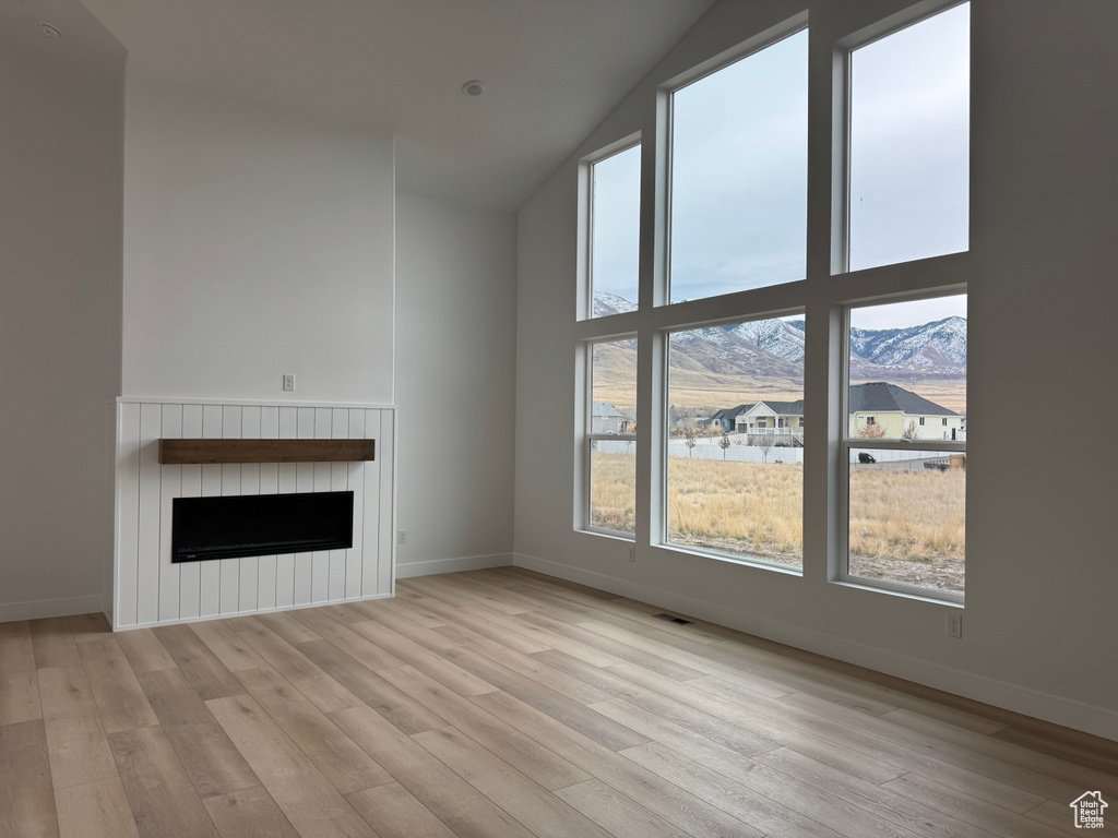 Unfurnished living room with a mountain view, vaulted ceiling, and light hardwood / wood-style flooring