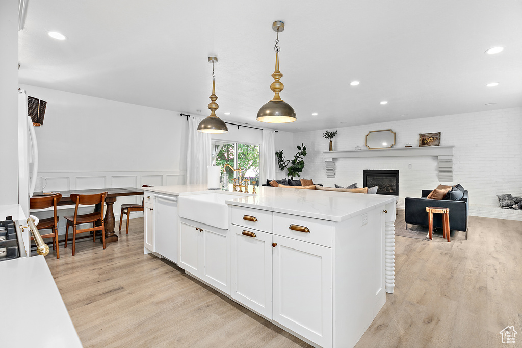 Kitchen with decorative light fixtures, white cabinetry, an island with sink, dishwasher, and light hardwood / wood-style floors