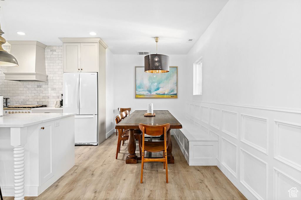 Kitchen with white fridge, premium range hood, hanging light fixtures, decorative backsplash, and light wood-type flooring