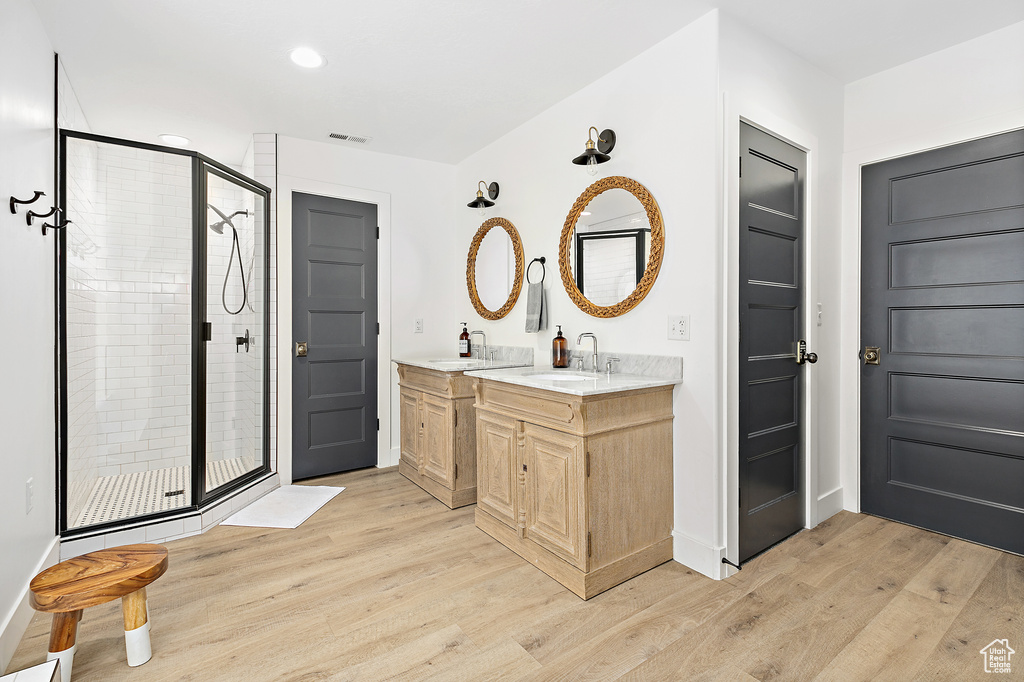 Bathroom with a shower with door, wood-type flooring, and double vanity