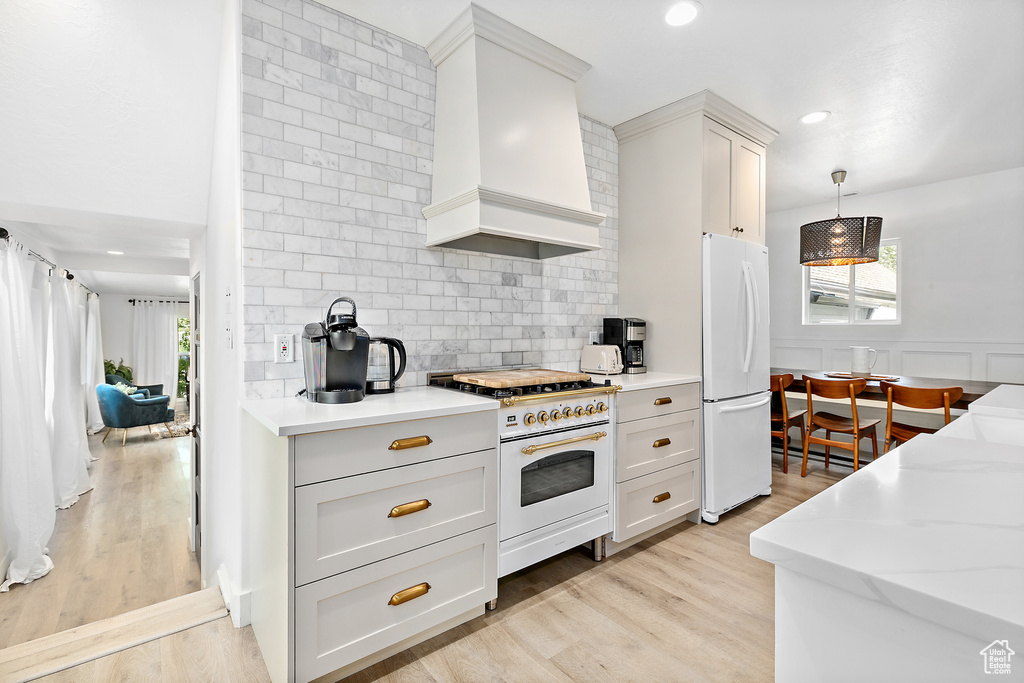 Kitchen with light hardwood / wood-style flooring, white appliances, premium range hood, backsplash, and decorative light fixtures