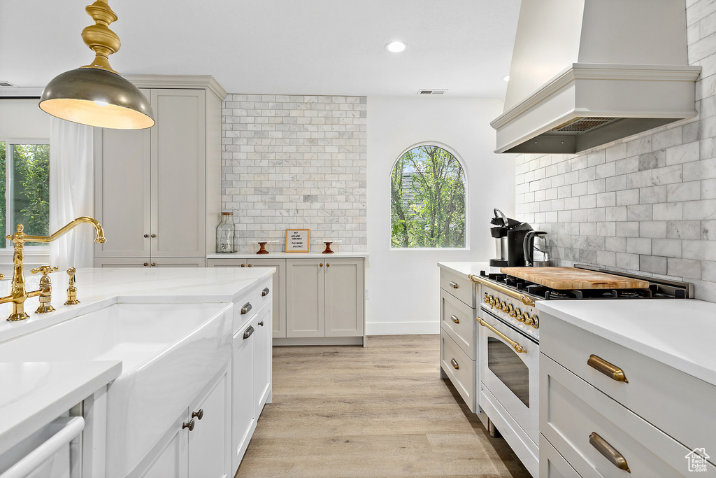 Kitchen featuring double oven range, decorative backsplash, a wealth of natural light, and custom range hood