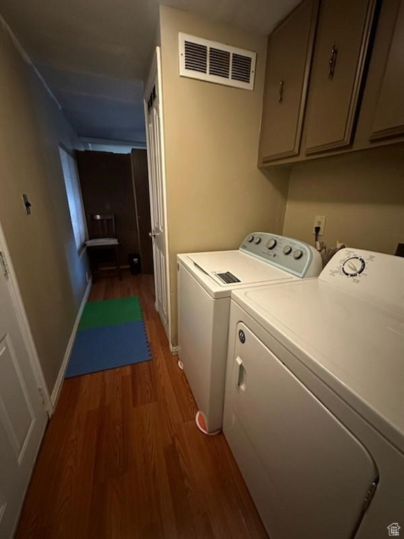 Washroom with independent washer and dryer, wood-type flooring, and cabinets