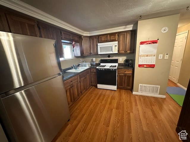 Kitchen with sink, white appliances, light wood-type flooring, and ornamental molding