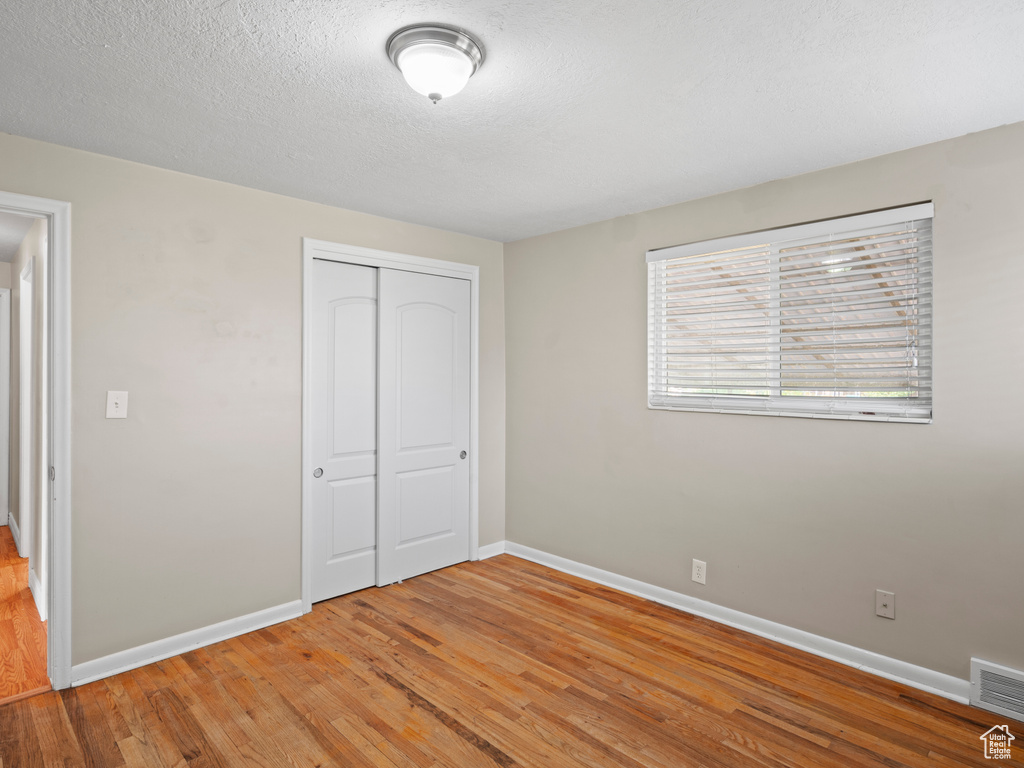 Unfurnished bedroom with a closet, a textured ceiling, and hardwood / wood-style flooring