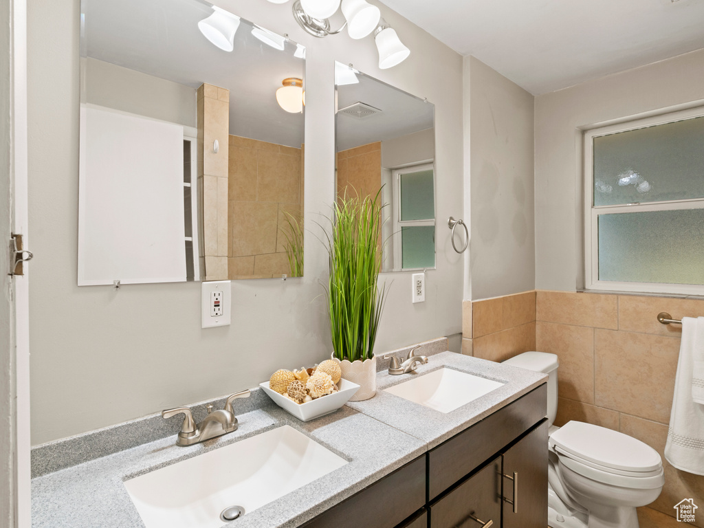 Bathroom with dual vanity, toilet, and tile walls