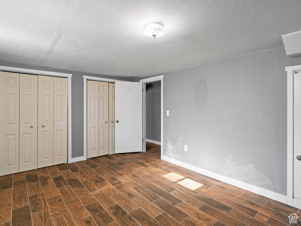 Unfurnished bedroom featuring multiple closets, a textured ceiling, and dark hardwood / wood-style flooring