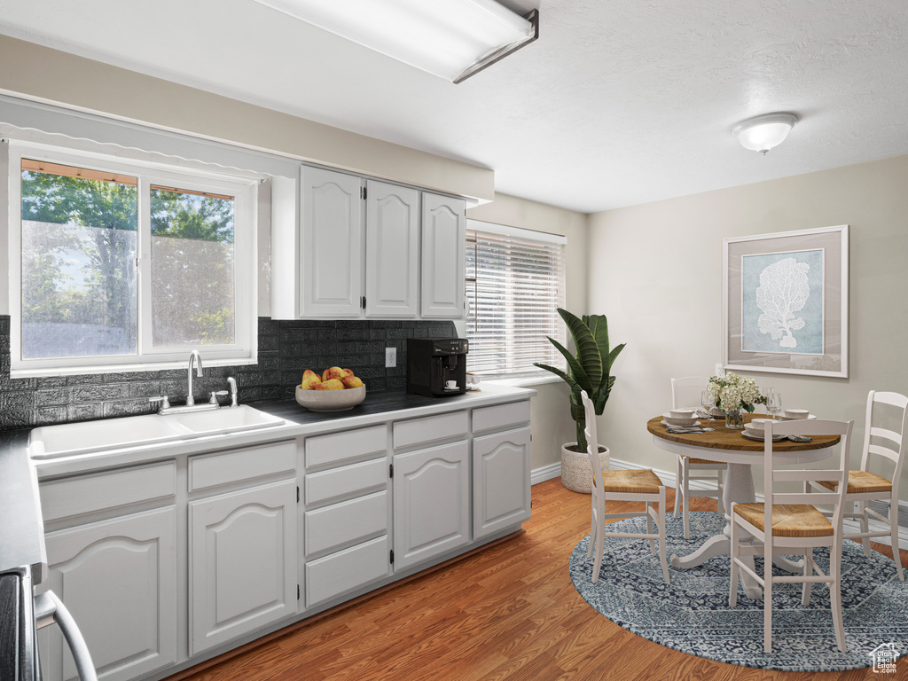 Kitchen featuring light hardwood / wood-style floors, white cabinetry, a healthy amount of sunlight, and backsplash