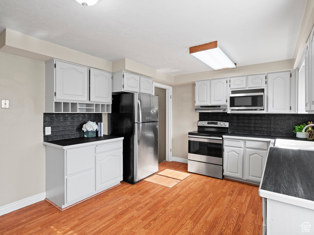 Kitchen with decorative backsplash, stainless steel appliances, light hardwood / wood-style flooring, and white cabinets