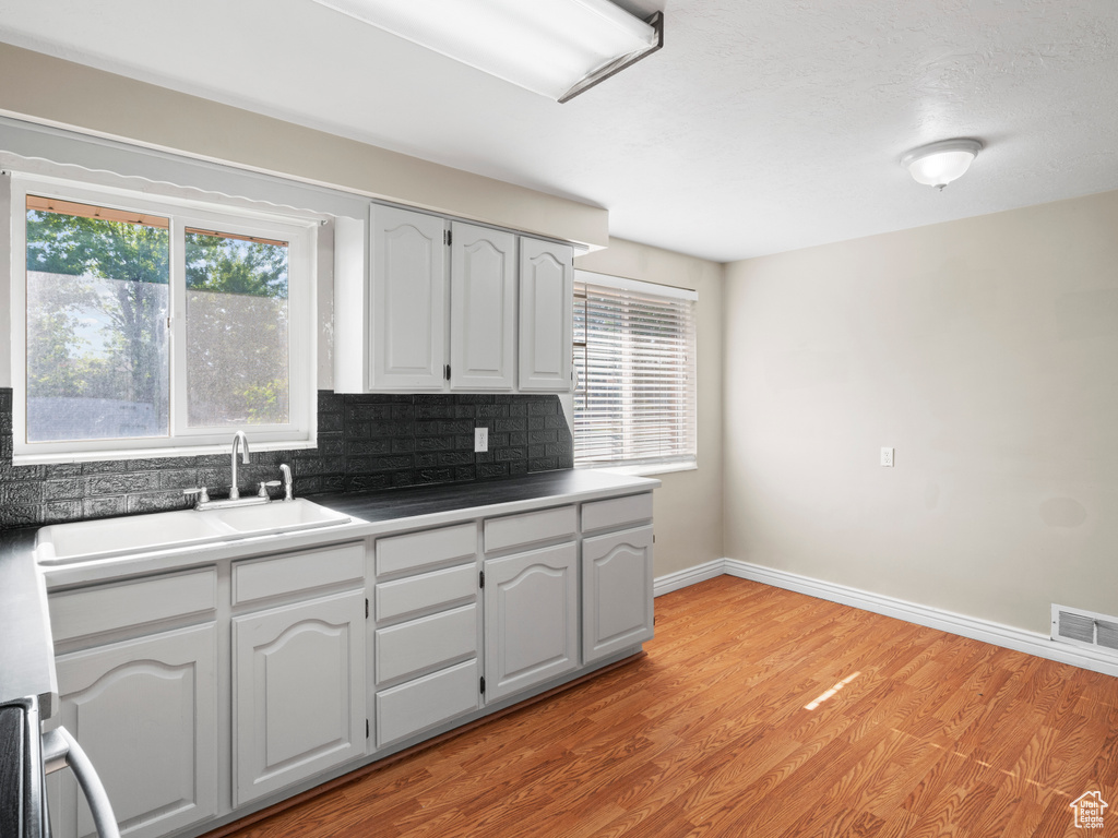 Kitchen with sink, a healthy amount of sunlight, tasteful backsplash, and light wood-type flooring