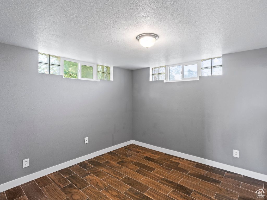 Basement featuring dark wood-type flooring, a textured ceiling, and plenty of natural light