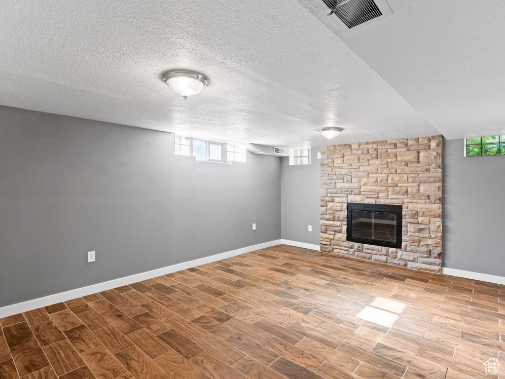 Unfurnished living room featuring a stone fireplace, a textured ceiling, and wood-type flooring