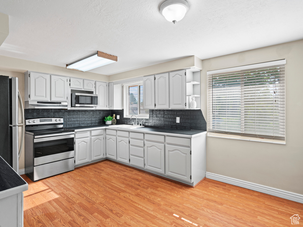 Kitchen featuring appliances with stainless steel finishes, light wood-type flooring, decorative backsplash, and plenty of natural light