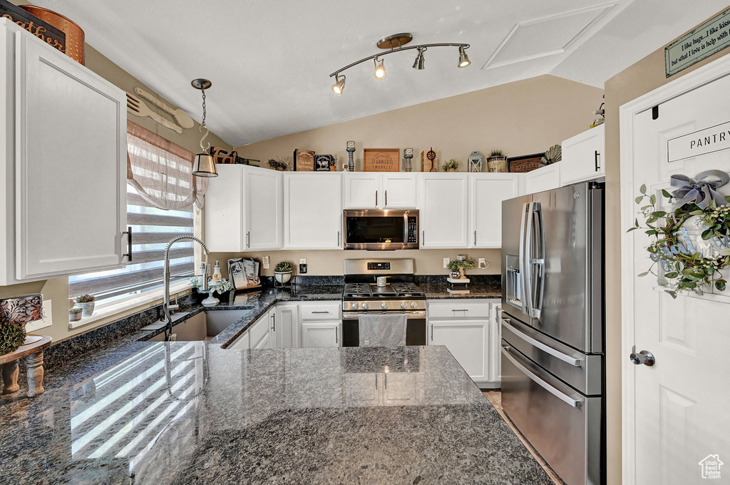 Kitchen featuring appliances with stainless steel finishes, track lighting, vaulted ceiling, sink, and dark stone countertops