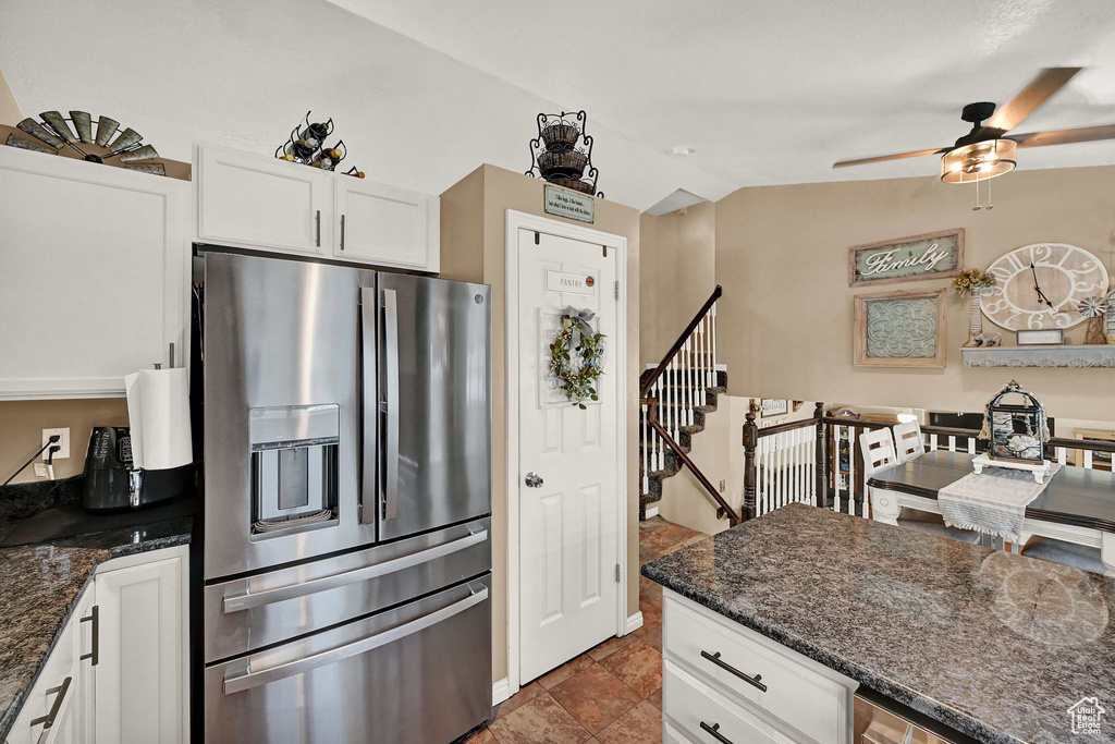 Kitchen featuring dark stone counters, dark tile patterned flooring, stainless steel refrigerator with ice dispenser, white cabinetry, and ceiling fan