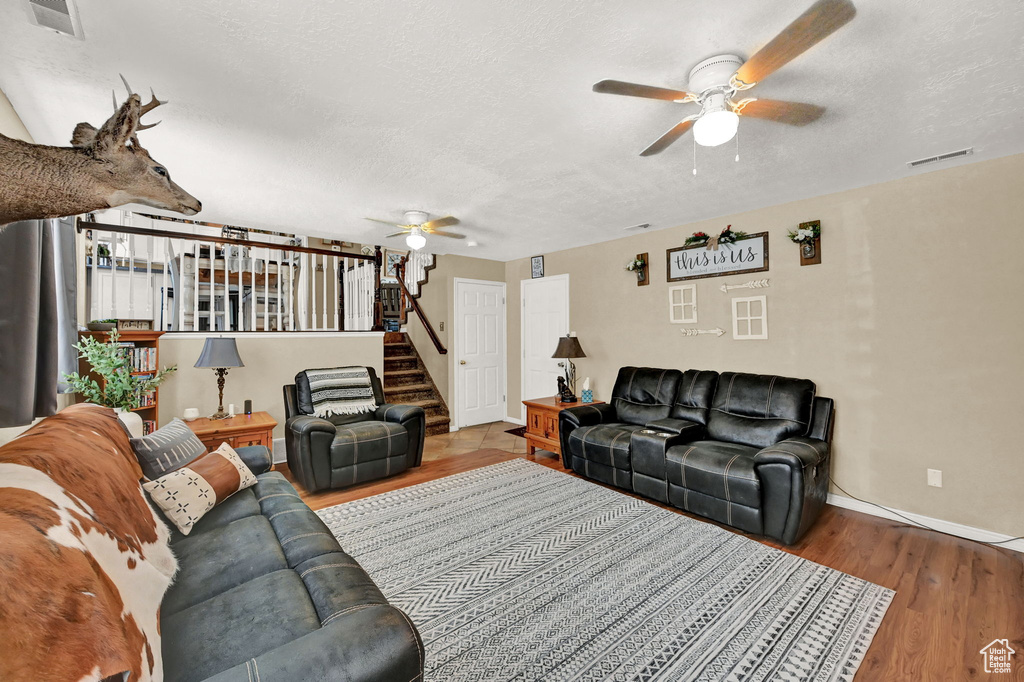 Living room with a textured ceiling, hardwood / wood-style flooring, and ceiling fan