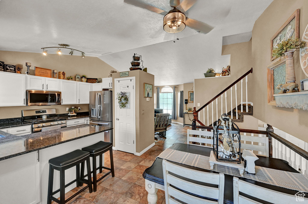 Kitchen featuring dark stone counters, tile patterned floors, stainless steel appliances, white cabinets, and rail lighting