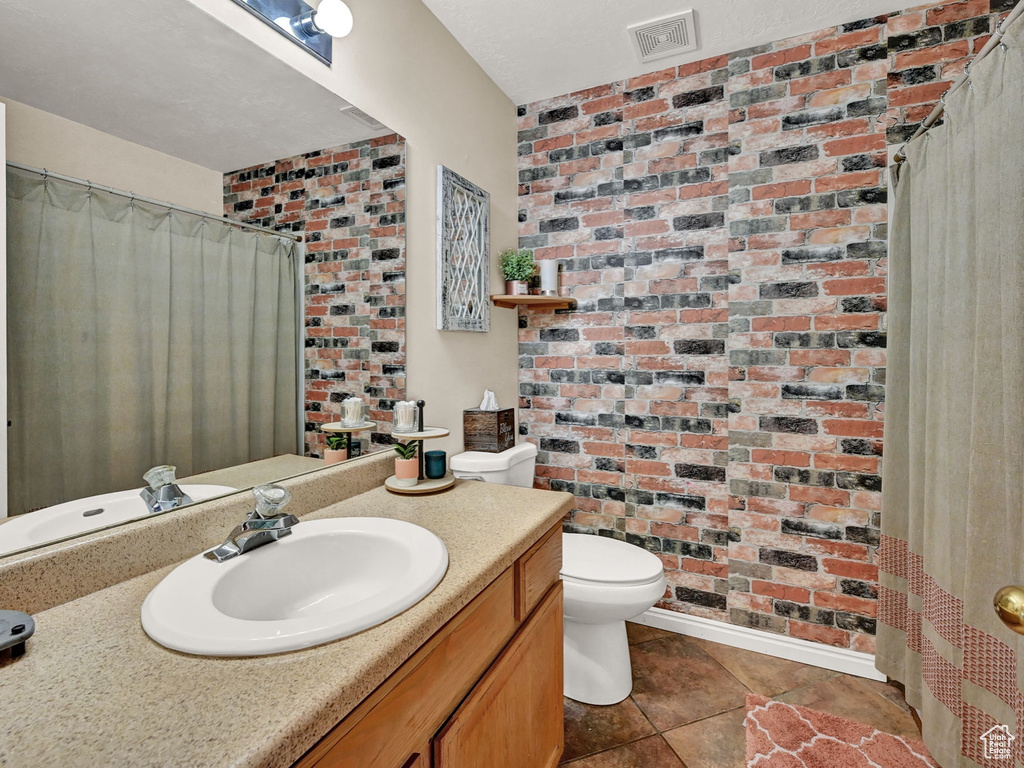 Bathroom with brick wall, tile patterned floors, toilet, and vanity