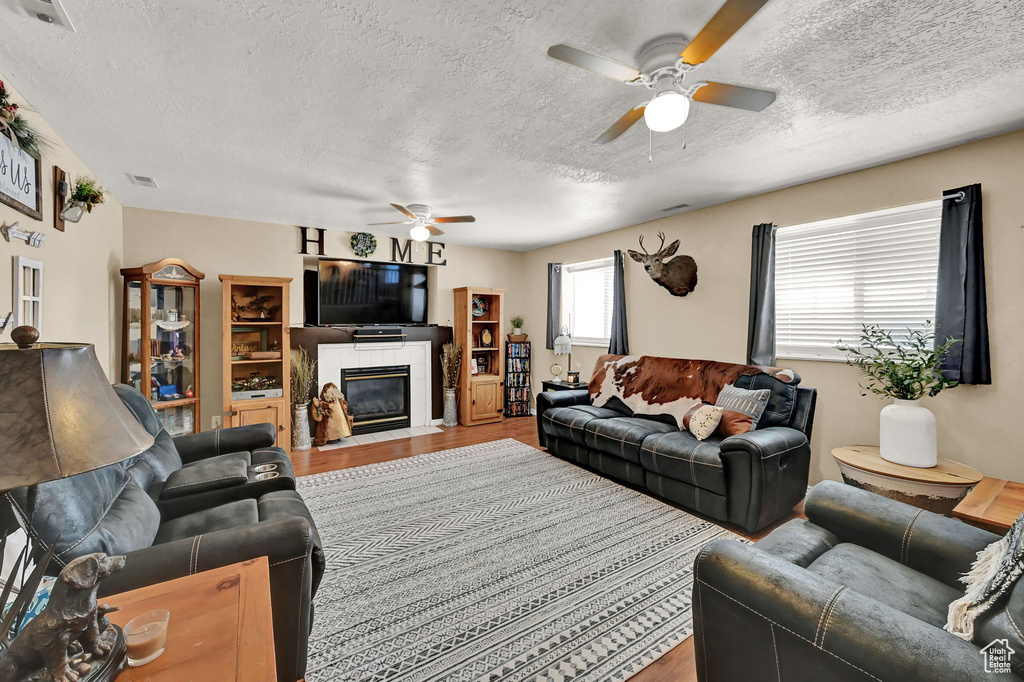 Living room featuring a textured ceiling, a tile fireplace, hardwood / wood-style floors, and ceiling fan