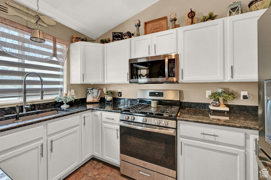 Kitchen with stainless steel appliances, white cabinets, sink, vaulted ceiling, and tile patterned flooring