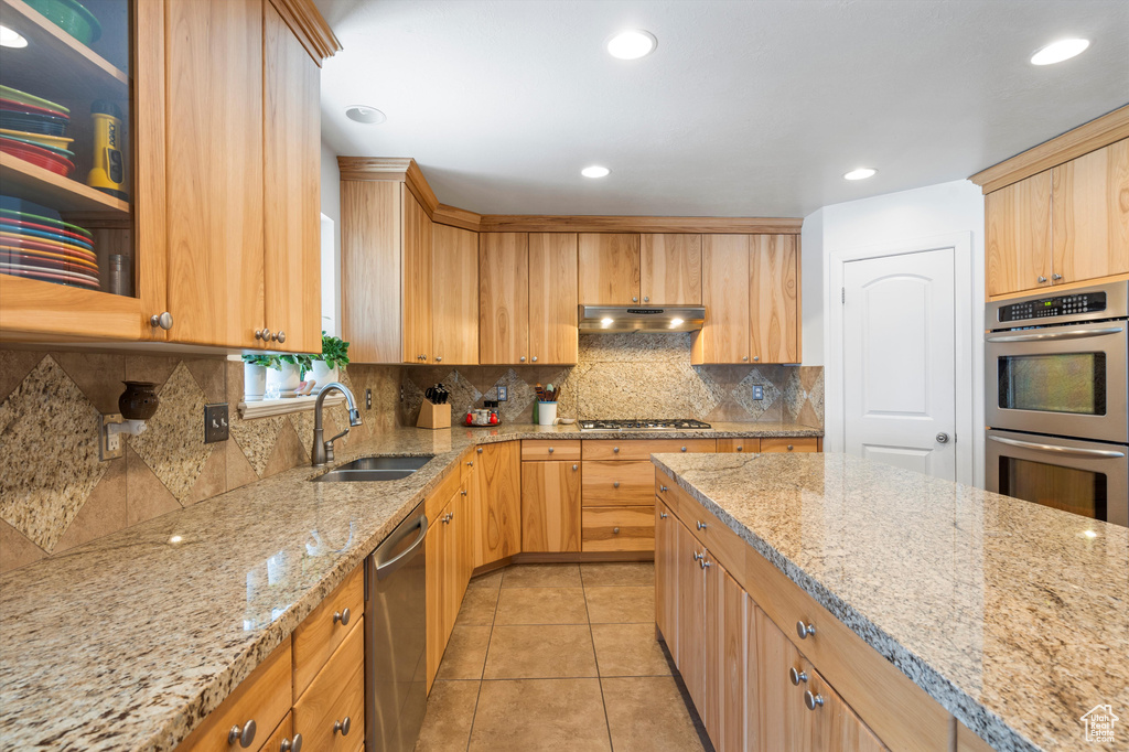 Kitchen featuring tasteful backsplash, light tile patterned floors, light stone countertops, appliances with stainless steel finishes, and sink