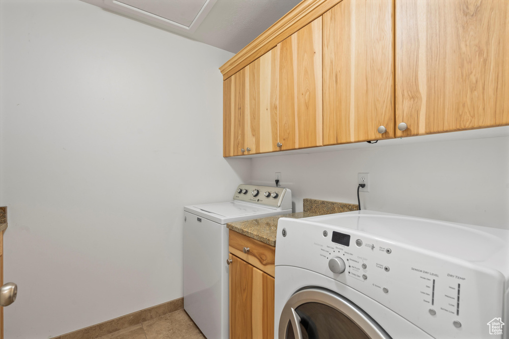 Laundry room with light tile patterned flooring, separate washer and dryer, and cabinets