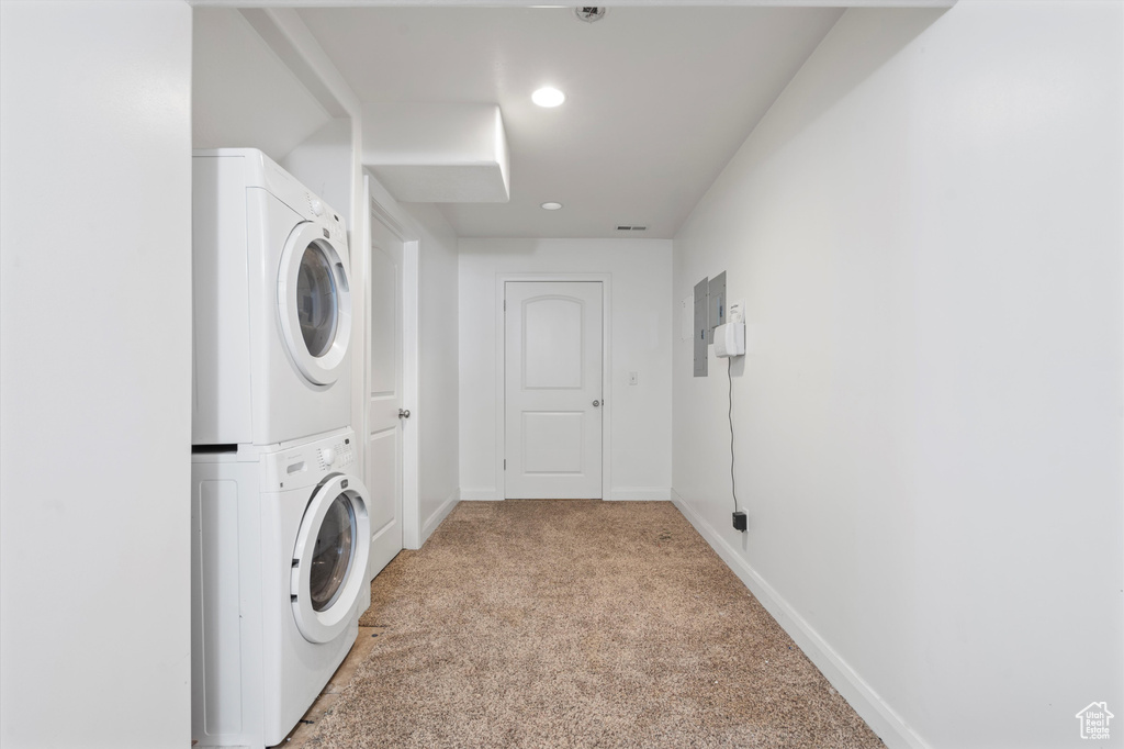 Laundry area with stacked washer and clothes dryer, light carpet, and electric panel