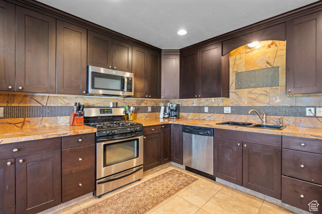 Kitchen with light tile patterned flooring, decorative backsplash, appliances with stainless steel finishes, and sink