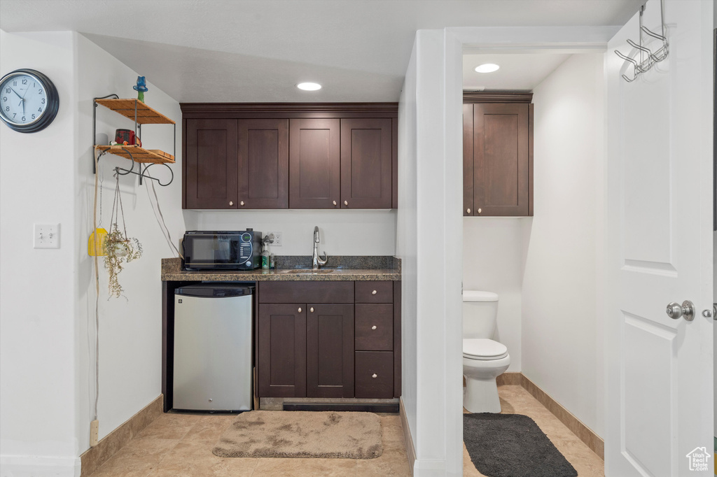 Kitchen with sink, dishwasher, light tile patterned floors, and dark brown cabinetry