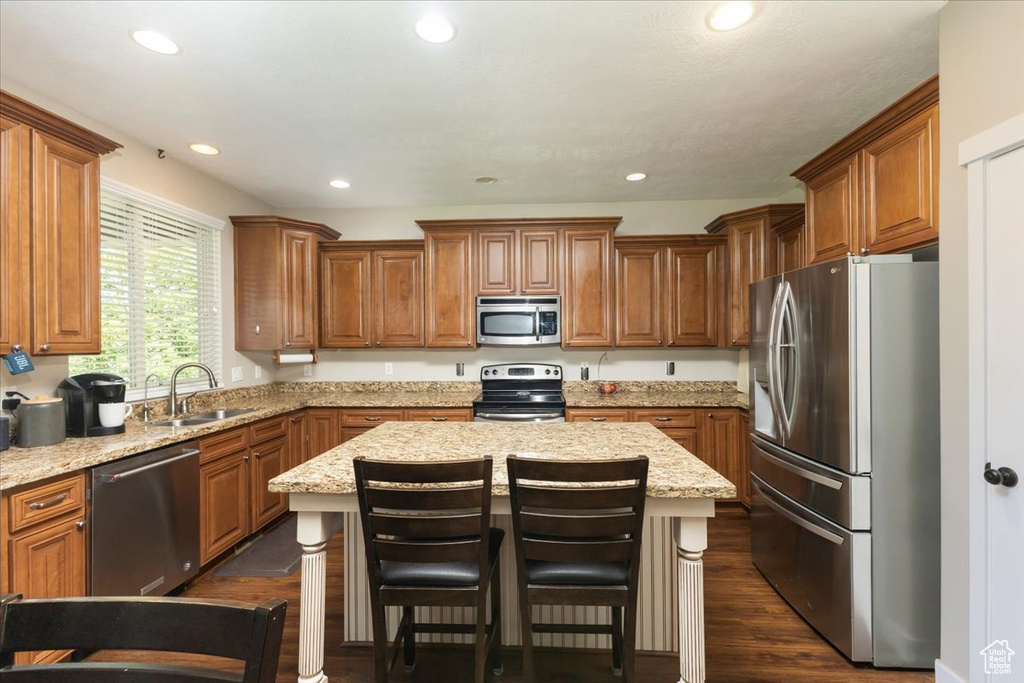 Kitchen with dark wood-type flooring, light stone counters, a kitchen island, stainless steel appliances, and sink