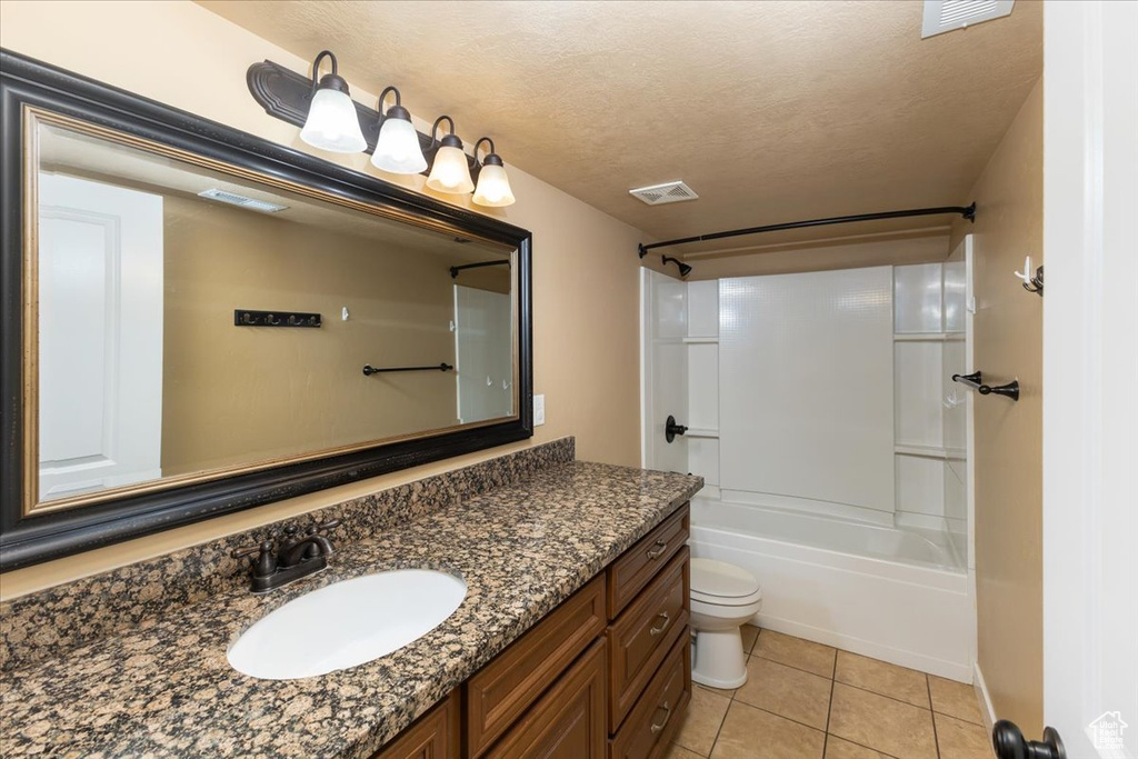 Full bathroom with a textured ceiling, toilet, vanity,  shower combination, and tile patterned floors