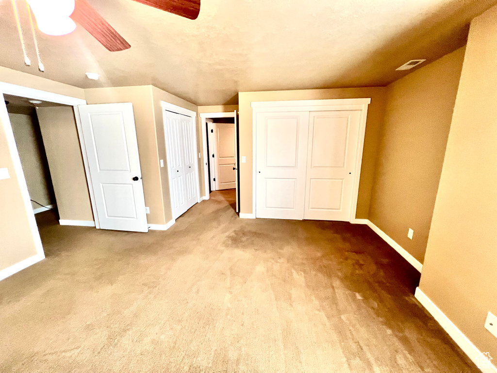 Unfurnished bedroom with ceiling fan, light colored carpet, and multiple closets