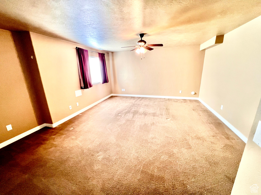 Empty room featuring a textured ceiling, carpet flooring, and ceiling fan