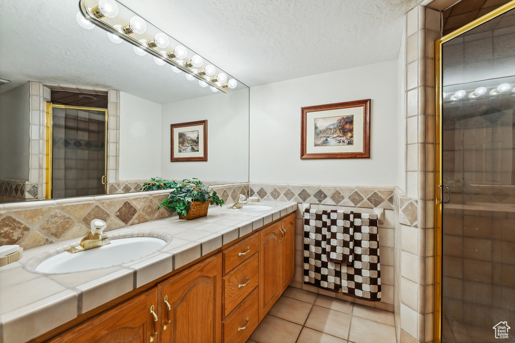 Bathroom featuring double vanity, an enclosed shower, tile walls, backsplash, and tile patterned floors