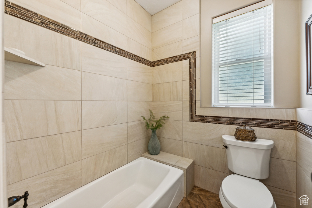 Bathroom with toilet, tile patterned floors, a healthy amount of sunlight, and tile walls