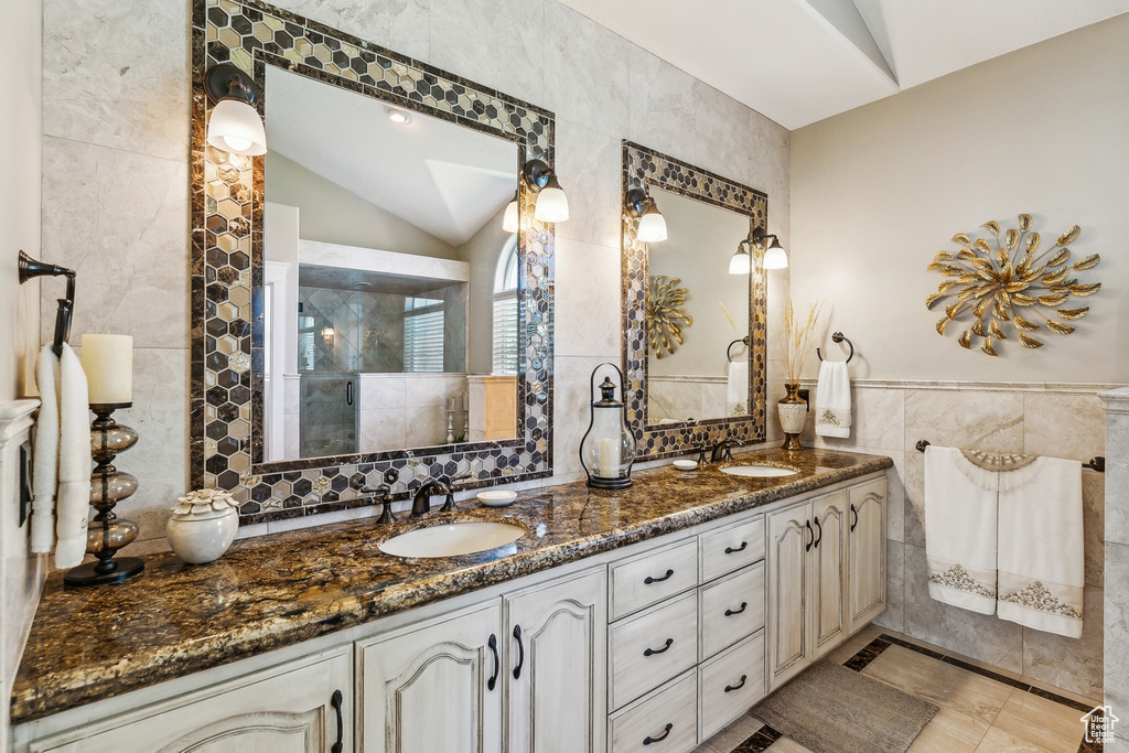 Bathroom with vaulted ceiling, tile patterned floors, tile walls, and dual bowl vanity