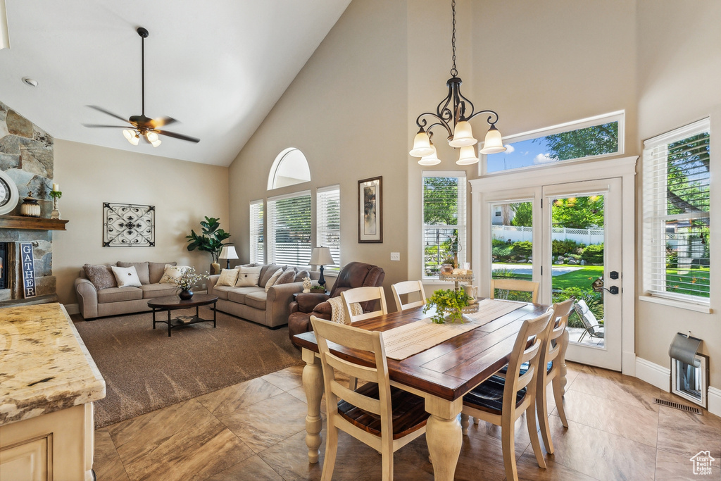 Tiled dining space featuring french doors, a healthy amount of sunlight, ceiling fan with notable chandelier, and high vaulted ceiling