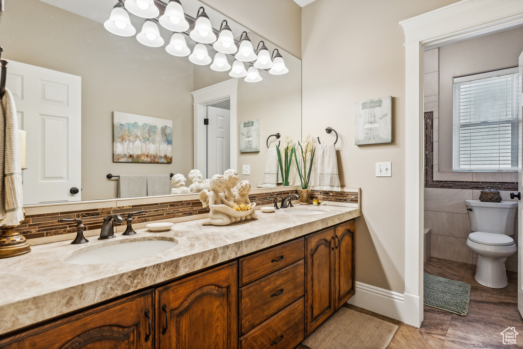 Bathroom featuring tile patterned flooring, tile walls, toilet, and double sink vanity