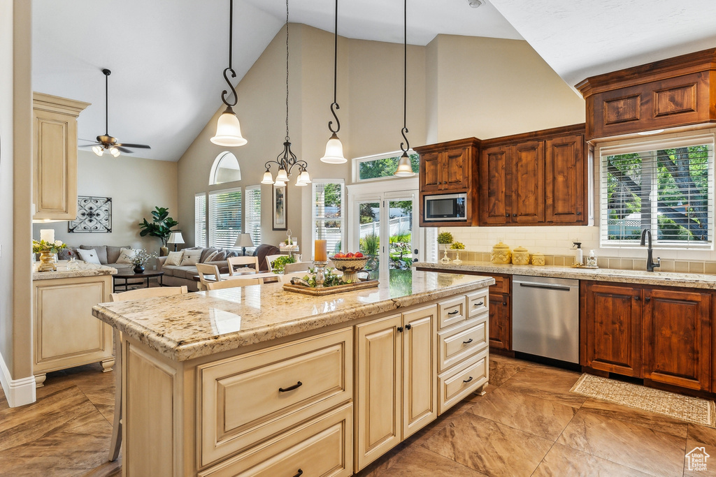 Kitchen featuring light tile patterned flooring, ceiling fan with notable chandelier, high vaulted ceiling, a kitchen island, and appliances with stainless steel finishes