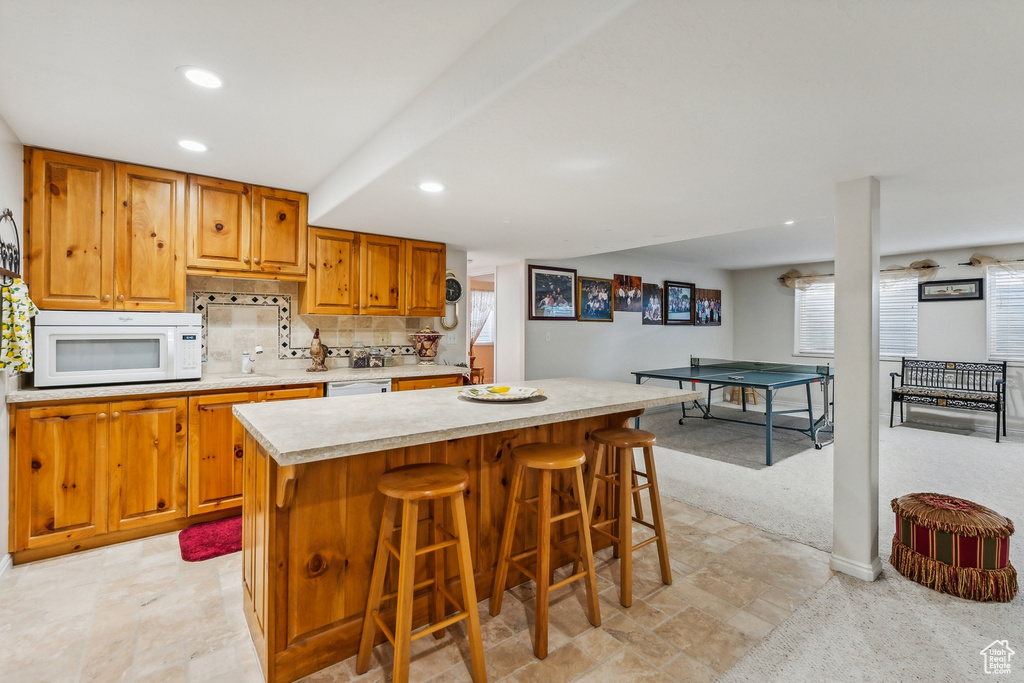 Kitchen featuring white appliances, light tile patterned floors, backsplash, a kitchen island, and a kitchen bar