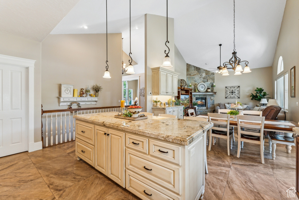 Kitchen with a stone fireplace, decorative light fixtures, light tile patterned floors, light stone countertops, and a center island