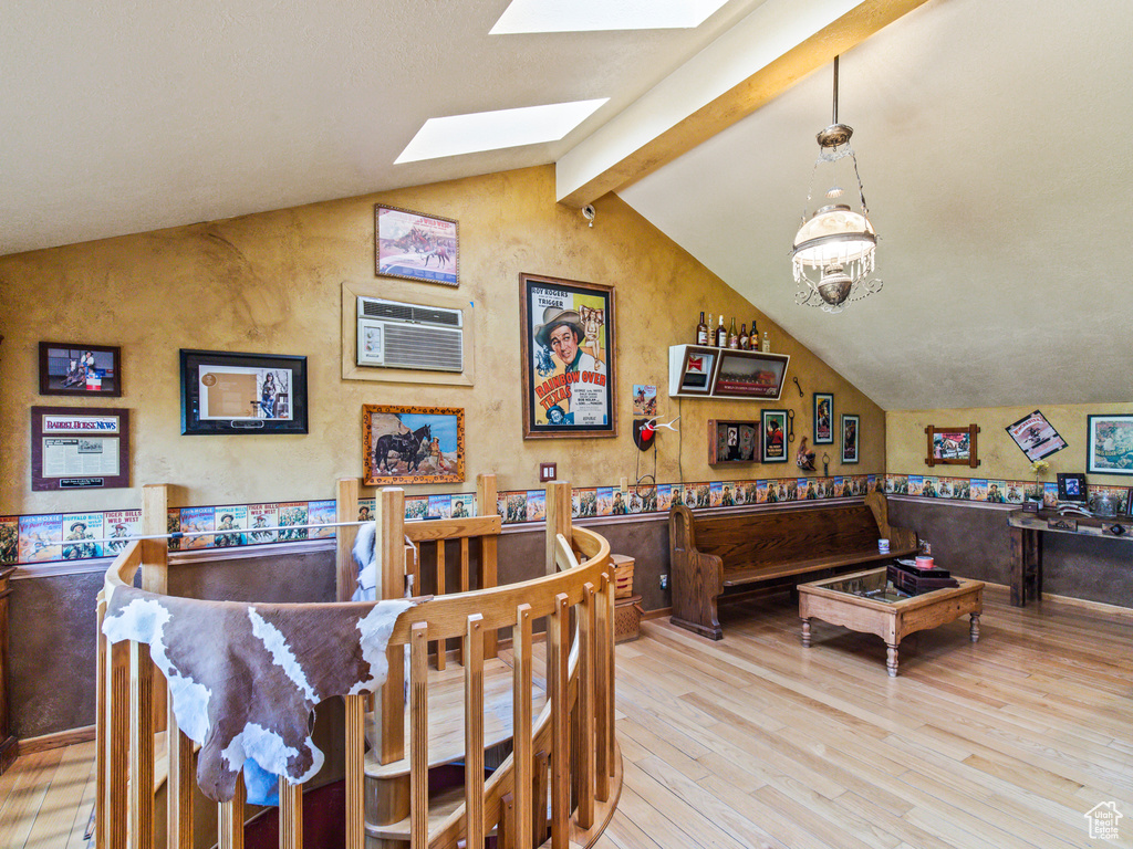 Dining area featuring lofted ceiling with skylight, a wall mounted air conditioner, light wood-type flooring, and an inviting chandelier