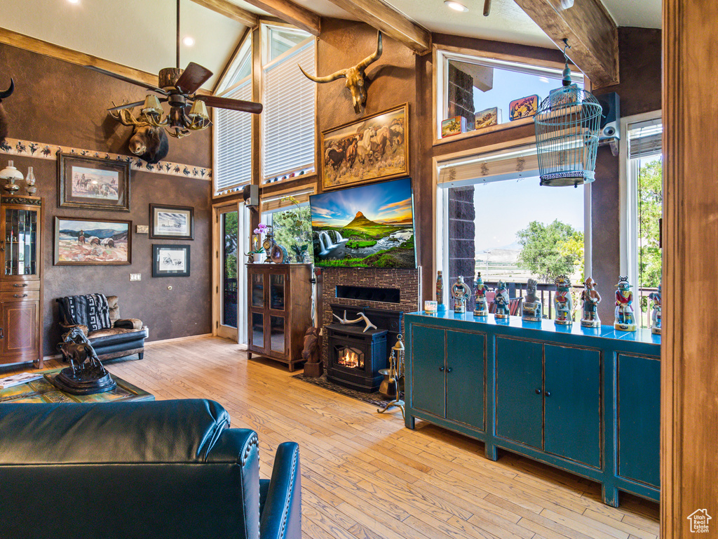 Living room featuring a fireplace, ceiling fan, a wood stove, light wood-type flooring, and beamed ceiling