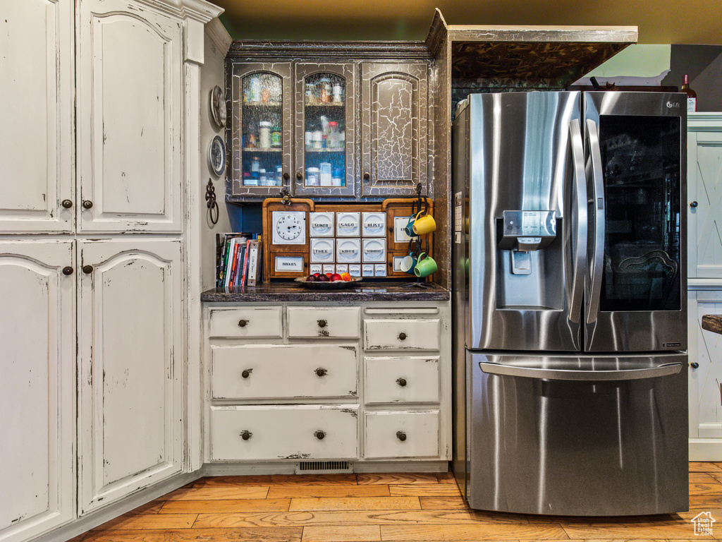 Kitchen with white cabinets, light wood-type flooring, and stainless steel refrigerator with ice dispenser