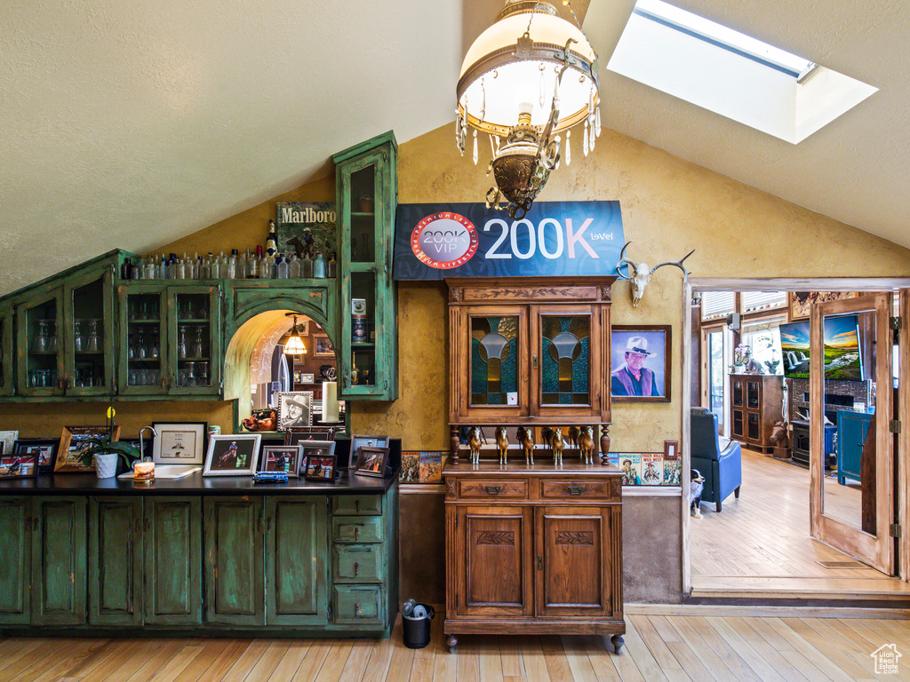 Bar featuring green cabinetry, vaulted ceiling with skylight, and light wood-type flooring