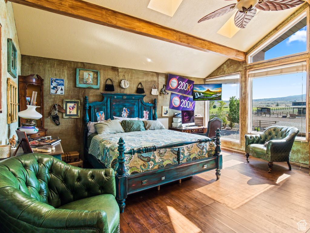 Bedroom featuring wooden walls, lofted ceiling with skylight, hardwood / wood-style floors, and ceiling fan