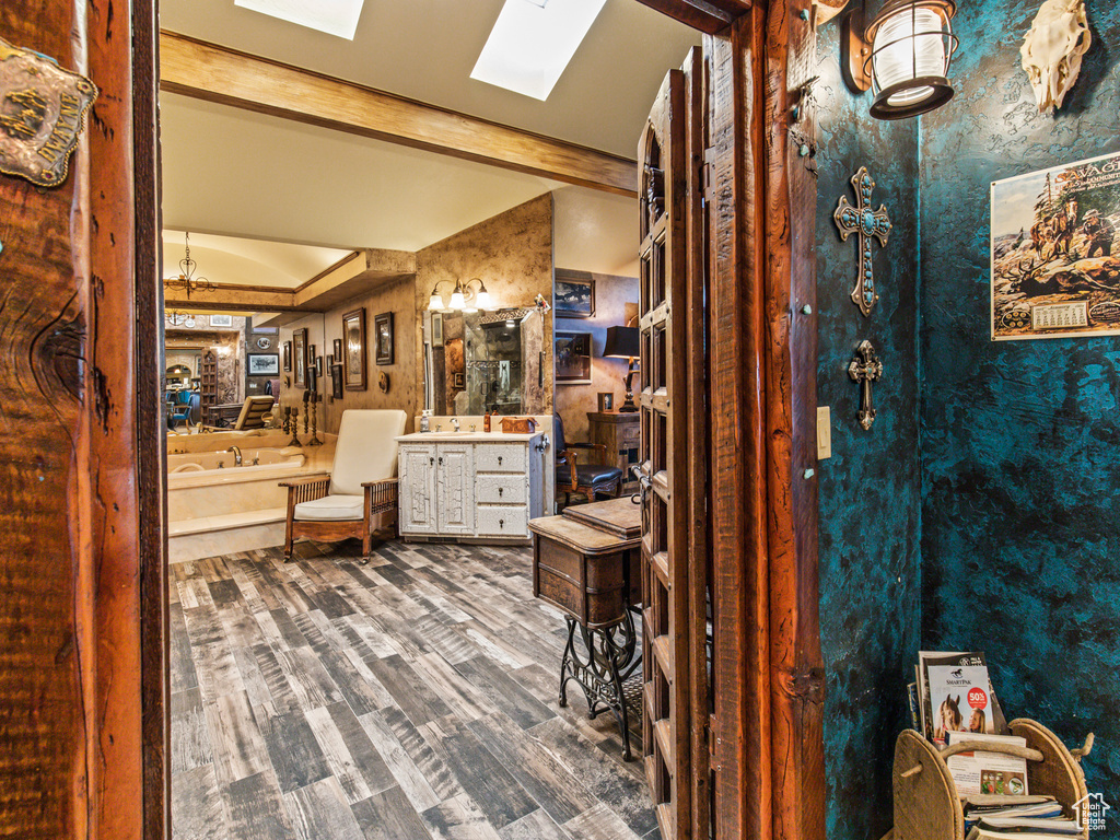 Bathroom featuring a tub, hardwood / wood-style floors, vanity, and vaulted ceiling with skylight