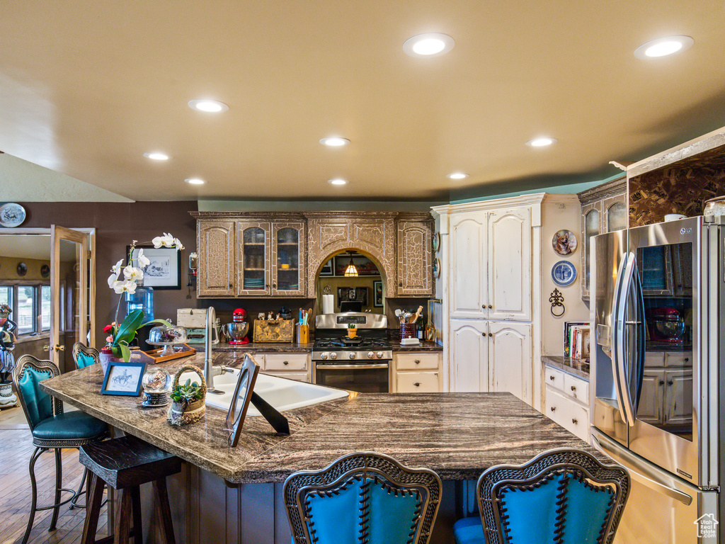 Kitchen featuring premium range hood, wood-type flooring, stainless steel appliances, a kitchen bar, and a center island with sink