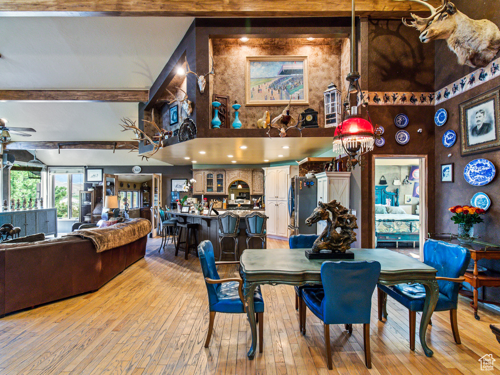 Dining room with beamed ceiling, light wood-type flooring, ceiling fan, and a towering ceiling